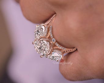 May include: Rose gold engagement ring with three large, clear, oval-cut diamonds and smaller accent diamonds. The ring has a detailed, ornate design with the text "Vitara Jewelry".