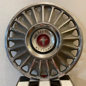 Puede incluir: Un tapacubos plateado y cromado con un logotipo de Mustang rojo y plateado. El tapacubos tiene un diseño de estrella con 16 radios.