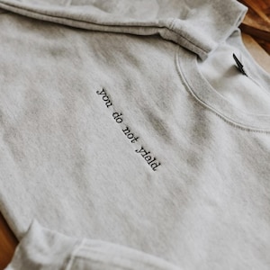 May include: A gray sweatshirt with the text "you do not yield" embroidered on the front.