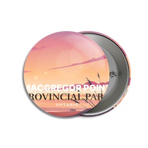 Könnte beinhalten: Ein runder Button mit einem Sonnenuntergangsdesign in Rosa-, Orange- und Lilatönen. Der Button zeigt den Text "MacGregor Point Provincial Park Ontario" in Weiß. Silhouetten von Pflanzen sind sichtbar.