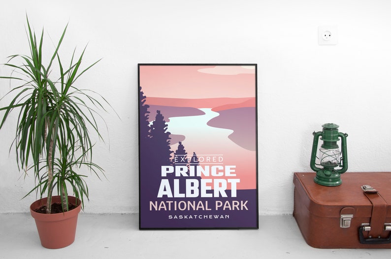 May include: A framed poster with a landscape design featuring a river and trees, with text that reads "EXPLORED PRINCE ALBERT NATIONAL PARK SASKATCHEWAN". A green lantern and a brown suitcase are next to the poster. A potted plant is on the left.