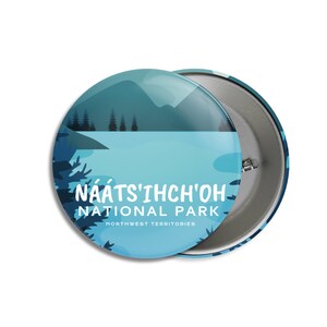 May include: A round button with a scenic illustration of a lake and mountains in shades of blue and green. The text "NAATS'IHCH'OH NATIONAL PARK NORTHWEST TERRITORIES" is displayed in white. The button has a metal backing.