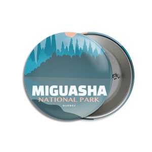 May include: A round button with a scenic design featuring a teal and blue landscape with trees, a lake, and a peach-colored sun. The text "Miguasha National Park Quebec" is printed in white and peach.