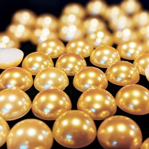 May include: A group of round, pearl-like embellishments in a golden color. The embellishments are arranged in a semi-circle pattern on a black surface.