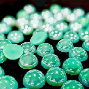 May include: A close-up of a group of iridescent green cabochons, some with a flat back, on a black surface.