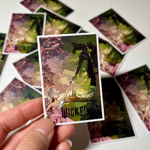 May include: A sticker featuring a colorful illustration of a green witch and a woman in a pink dress. The witch is holding out her hand to the woman, and the background is a green and pink landscape. The sticker says "Wicked" at the bottom.