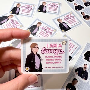 May include: A selection of stickers with a cartoon illustration of a person wearing glasses, a stethoscope, and a black jacket. The stickers have the text "I AM A Savage" and other phrases. The stickers are white with a light blue border.