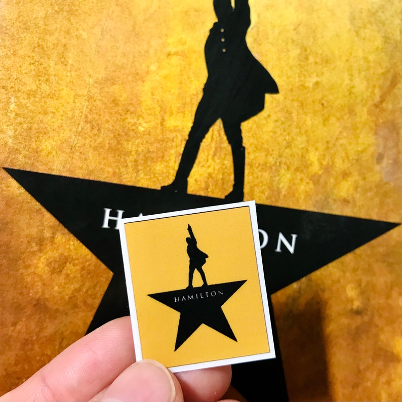 May include: A yellow sticker with a black silhouette of a person standing on a black star with the word "HAMILTON" written on it.