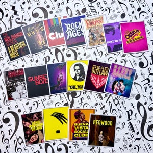 May include: A collection of colorful musical theater show stickers, including "The Neil Diamond Musical," "Rock of Ages," and "Charlie and the Chocolate Factory." The stickers are arranged on a background of musical notes.