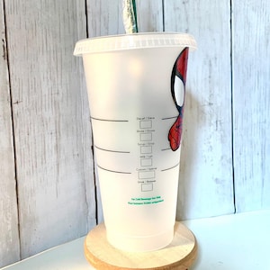 May include: A white reusable cup with a black and white label that says "Decaf/D&eacute;ca", "Shots/Doses", "Syrup/Sirop", "Milk/Lait", "Custom/Sp&eacute;cial", "Drink/Boisson", and "For Cold Beverage Use Only". The cup has a red and black Spiderman design on the side.