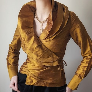 May include: A gold satin wrap blouse with a large ruffled collar and long sleeves. The blouse has a tie at the waist.