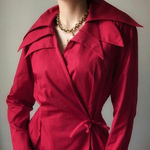 May include: A red wrap dress with a large, dramatic collar. The collar has multiple points and is folded over. The dress has long sleeves and a tie at the waist.