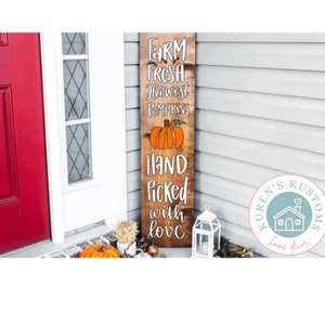 May include: A wooden sign with the text "FARM FRESH Harvest PUMPKINS HAND Picked with love" and a pumpkin graphic. The sign is leaning against a red door and a white lantern.