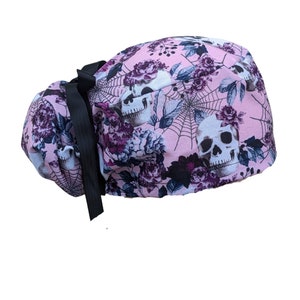 May include: A pink surgical scrub hat with a skull and floral print. The hat has a black ribbon tie.