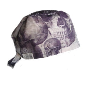 May include: A beige scrub hat with a skull and bones print. The print features a detailed anatomical illustration of a human skull.