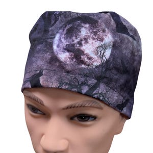 May include: A fitted fabric cap featuring a dark purple and black print of a full moon, silhouetted bare trees, and flying bats. The head covering has a wide, stitched band at the base and a rounded crown, displaying a nocturnal scene.