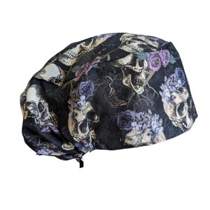 May include: Black scrub cap with a skull and floral print. The skulls are surrounded by purple flowers and vines.