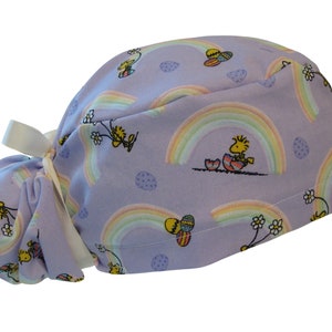 May include: Purple scrub hat with a tie, featuring a repeating pattern of rainbows, Easter eggs, and cartoon birds.