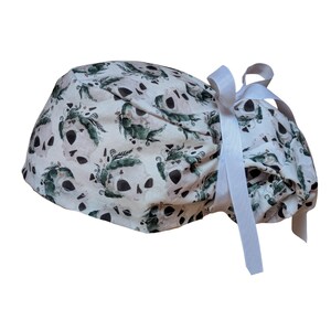 May include: A white skull cap with a repeating pattern of skulls and green floral accents. The cap has a white ribbon tie. The skull cap is a medical or surgical cap.