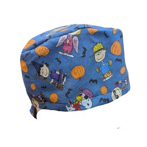 May include: Blue scrub cap featuring a Halloween-themed pattern with cartoon characters, pumpkins, and bats. The cap is made of a soft fabric and is designed to fit comfortably. Perfect for healthcare professionals or anyone wanting a festive touch.