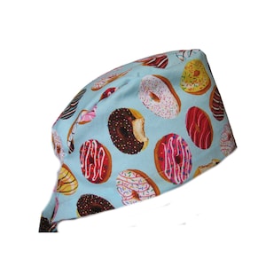 May include: A light blue surgical scrub hat with a donut pattern. The donuts are various colors and have different toppings, including sprinkles, chocolate, and frosting.