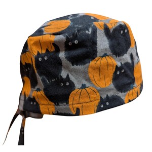 May include: A Halloween-themed scrub cap featuring a repeating pattern of black cats and orange pumpkins on a gray background. The cap has ties for an adjustable fit and is made of a soft fabric.