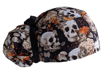 May include: Black scrub hat with a skull and floral print. The hat has a black tie and is made of a soft, comfortable fabric.