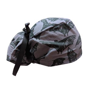 May include: Gray scrub cap with a black bat pattern. The cap has a black ribbon tie in the back. The bats are drawn in a sketchy style, with their wings spread. The fabric is a soft, light gray color.
