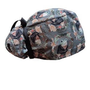 May include: A gray scrub cap with a whimsical pattern of frogs, mushrooms, and flowers. The cap has a black ribbon tie and is designed for medical professionals or those in the healthcare field.
