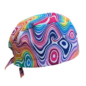 May include: A colorful surgical scrub cap with a vibrant, swirling pattern in shades of red, orange, yellow, green, blue, and purple. The cap has a tie closure at the back and is made of a soft, patterned fabric.