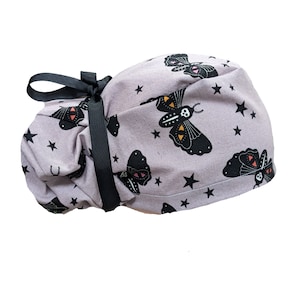 May include: A purple scrub hat with a black ribbon tie and a repeating pattern of black moths with orange and yellow accents on a background of small white stars.