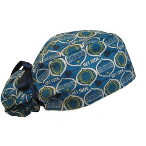 May include: Blue and yellow patterned surgical scrub hat with a navy blue ribbon. The hat has a repeating pattern of flowers, guitars, and the words "Hey Jude" and "Don't make it sad, take it slow and make it better".