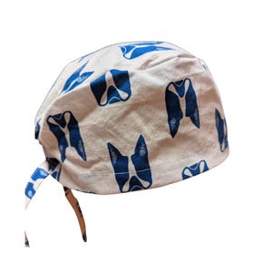 May include: A white surgical scrub cap with a repeating pattern of blue tooth illustrations. The cap has a tie closure in the back and is made of a soft, lightweight fabric. Ideal for dental professionals.
