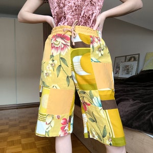 Può includere: Shorts patchwork gialli, marroni e bianchi con stampa floreale. I pantaloncini hanno una vita con coulisse e sono realizzati in un tessuto leggero.