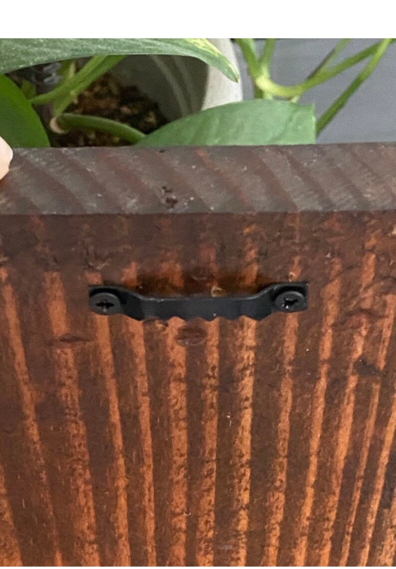 May include: A close-up of a dark brown wooden sign with a black metal hanging bracket attached to the back. The bracket has two screws visible.