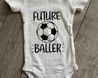 May include: White baby onesie with black text that reads "FUTURE BALLER" and a black and white soccer ball graphic.