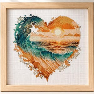 May include: A square wooden frame containing a cross-stitch embroidery piece. The needlework depicts a heart-shaped scene featuring a large teal and blue ocean wave crashing on the left side, transitioning into a warm orange sunset over the sea.