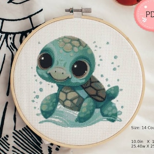 Puede incluir: Un bordado de punto de cruz de una tortuga turquesa con grandes ojos negros, en un aro de madera. La tortuga est&aacute; representada en un estilo de dibujos animados, con un caparaz&oacute;n estampado y una expresi&oacute;n sonriente. La pieza mide 25,4 cm por 25,4 cm.