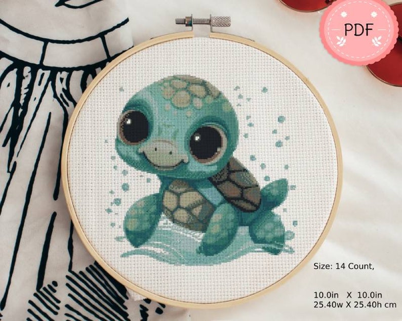 Puede incluir: Un bordado de punto de cruz de una tortuga turquesa con grandes ojos negros, en un aro de madera. La tortuga est&aacute; representada en un estilo de dibujos animados, con un caparaz&oacute;n estampado y una expresi&oacute;n sonriente. La pieza mide 25,4 cm por 25,4 cm.