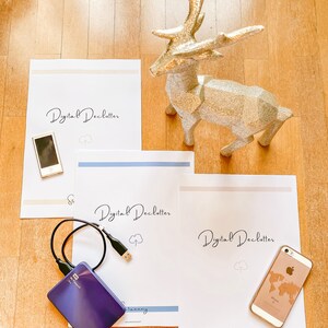 Puede incluir: Una figura de reno con purpurina dorada se encuentra cerca de hojas de papel blancas con el texto "Digital Declutter" y un disco duro externo morado. También hay un iPhone dorado y un iPod.