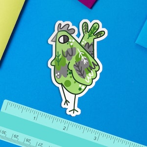 Puede incluir: Un pollo de dibujos animados verde y gris con hojas y ramas en su cuerpo. El pollo está de pie sobre un fondo azul.