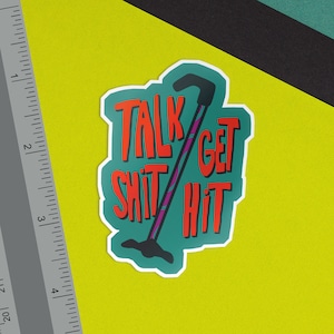 May include: A teal green sticker with a white border featuring a black and purple walking stick with the text "Talk Shit Get Hit" in red.