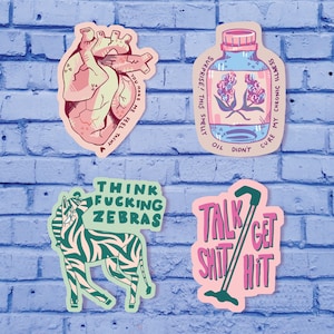 May include: Four colorful stickers with humorous text and illustrations. The first sticker features a pink heart with the text "You make me feel tachy". The second sticker features a blue bottle with flowers and the text "Surprise! This smelly oil didn't cure my chronic illness". The third sticker features a green zebra with the text "Think Fucking Zebras". The fourth sticker features a pink and green stick figure with the text "Talk Shit/Get Hit".