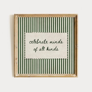 May include: A square wooden frame containing a dark green and white vertical striped background. Centered is a cream-colored rectangular paper with scalloped edges featuring the black handwritten text, celebrate minds of all kinds.