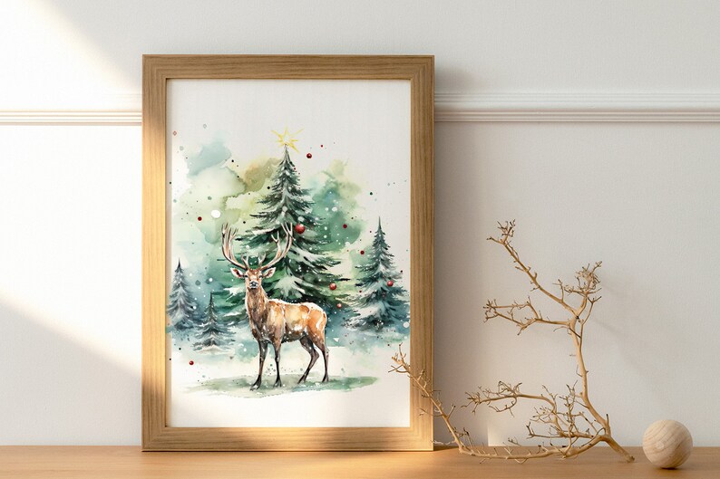 以下が含まれることがあります： 雪の降る森にいる鹿を描いた、額入りの水彩画。クリスマスツリーが描かれています。フレームは明るい茶色の木製です。赤いオーナメントと星が木を飾っています。全体的な配色は緑、茶色、白です。