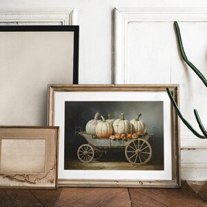 May include: A framed painting of a vintage wagon filled with white pumpkins and gourds. The wagon has wooden wheels and is set against a dark blue background.
