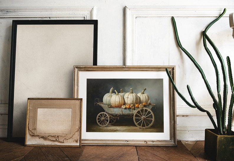 May include: A framed painting of a vintage wagon filled with white pumpkins and gourds. The wagon has wooden wheels and is set against a dark blue background.