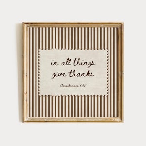 May include: A square wall art piece in a distressed gold frame featuring a brown and white vertical striped background. A central cream-colored rectangular paper with scalloped edges displays the brown text: in all things give thanks thessalonians 5:18.