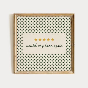 May include: A square framed print featuring a cream-coloured centre panel with five gold stars and the black text would cry here again. The border consists of a repeating pattern of small dark green polka dots on a cream background.