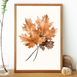 May include: A framed watercolour painting of two brown maple leaves on a white background.